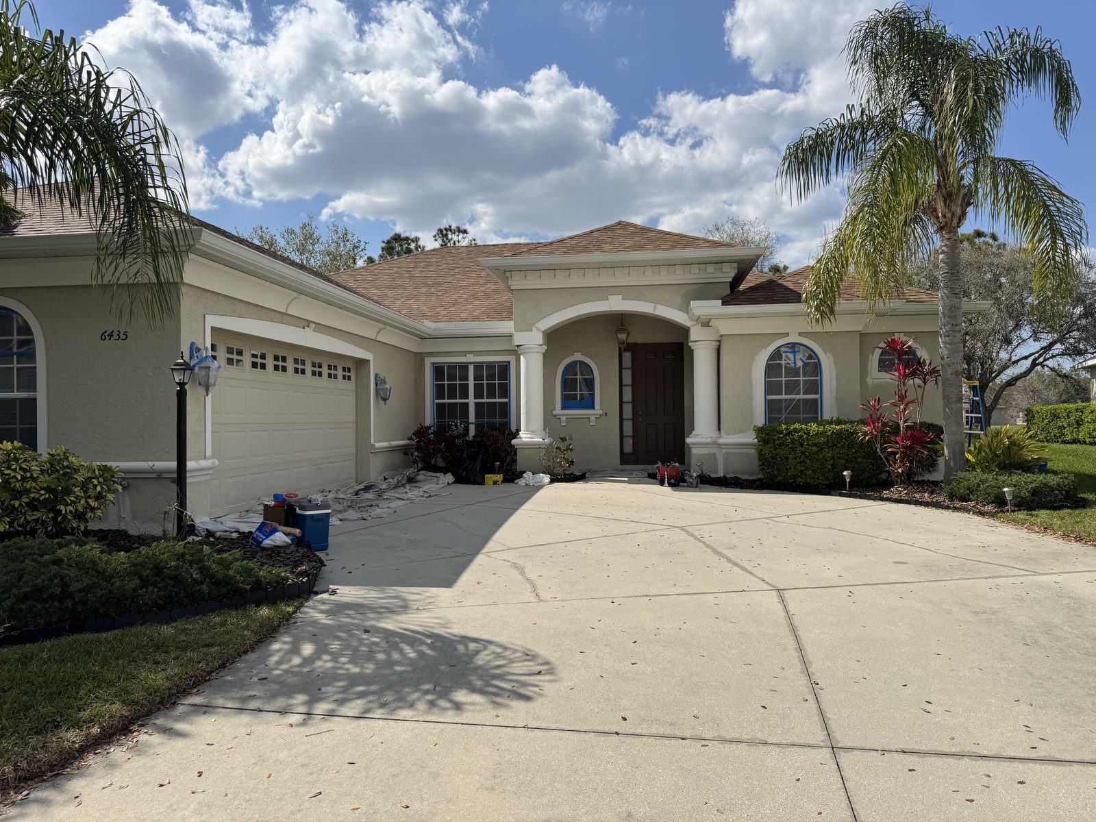 Tan single-story Florida home with a columned arched entry and palms, freshly painted