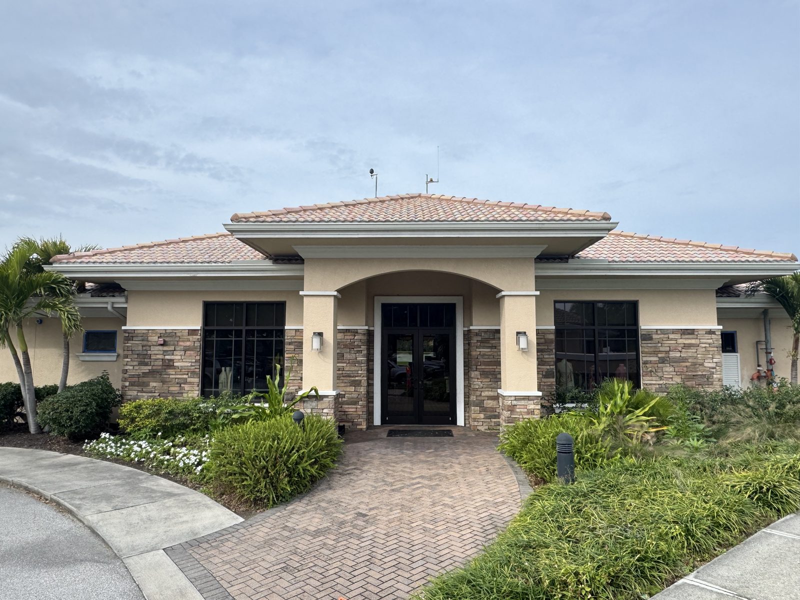 Tan single-story home with stone accents and an arched entry, freshly painted, with a paver driveway